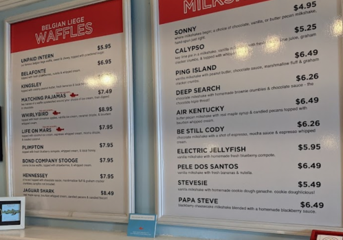 Menu board featuring Belgian Liege waffles and milkshakes with various creative names and prices.