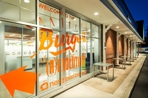 Exterior view of a burger restaurant with large orange lettering on glass windows, inviting customers inside.