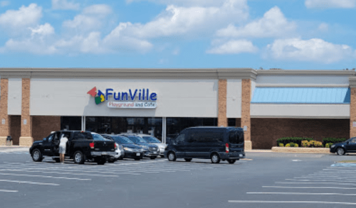 Exterior of FunVille Playground and Café, featuring a blue sky and parked cars in front of the building.