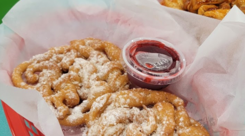 A red basket with two funnel cakes dusted with powdered sugar and a small cup of red sauce.