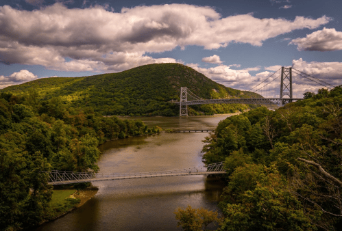 A scenic view of a river surrounded by green hills, featuring multiple bridges under a cloudy sky.