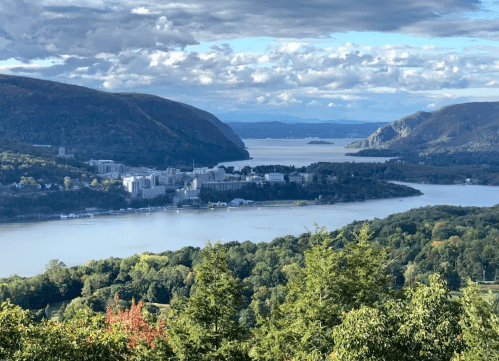 A scenic view of a river surrounded by mountains and trees under a partly cloudy sky.