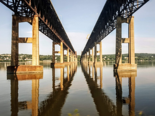 Two parallel bridges span over a calm river, reflecting their structures in the water below.