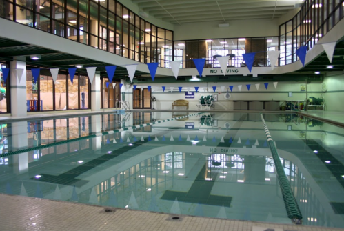 Indoor swimming pool with clear water, lane markers, and blue and white flags hanging above.