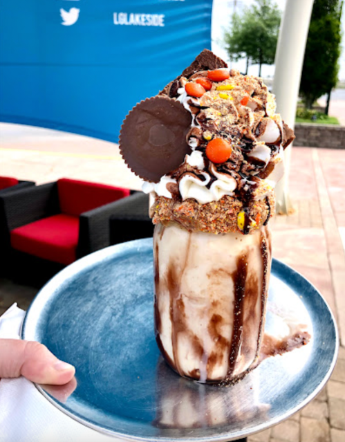 A tall milkshake topped with whipped cream, chocolate, candy, and a large cookie, served on a silver tray.