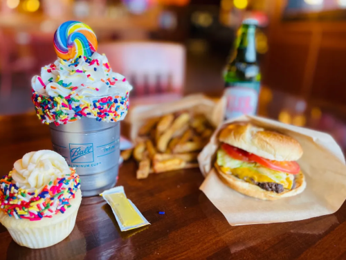 A colorful dessert, burger, and fries on a table, with a soda in a cup, all set in a casual dining environment.