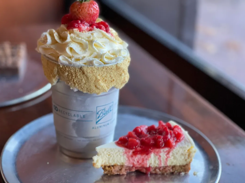 A milkshake topped with whipped cream and a strawberry, alongside a slice of cheesecake with strawberry topping.