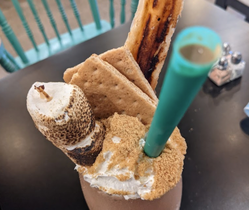 A decadent milkshake topped with toasted marshmallow, graham crackers, and a green straw.