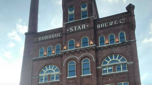 Historic brick building with "Dubuque Star Brewery" signage, featuring arched windows and a tall smokestack.