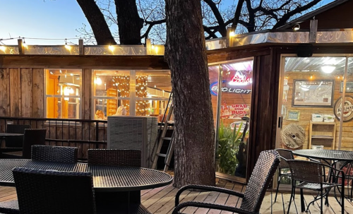 Cozy outdoor dining area with wooden decor, string lights, and tables near a rustic building at dusk.
