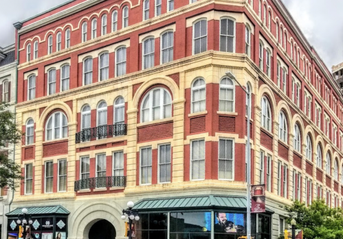 Historic red brick building with arched windows and decorative details, featuring a modern screen at the entrance.