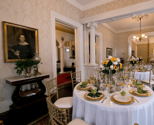 Elegant dining room set for a meal, featuring floral centerpieces and a portrait on the wall.