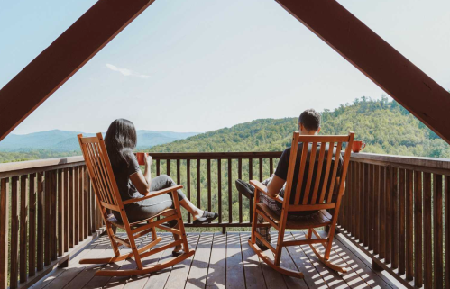 Two people relax in rocking chairs on a balcony, overlooking a scenic mountain view.