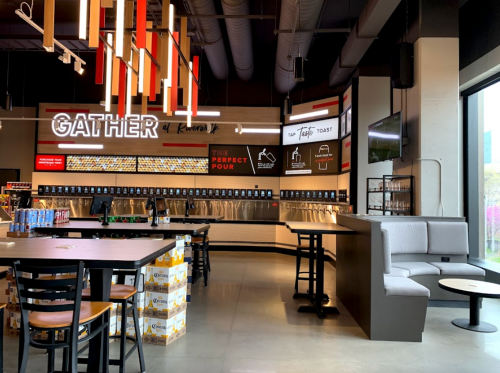 A modern bar interior with a self-serve drink station, seating areas, and vibrant decor featuring the word "GATHER."