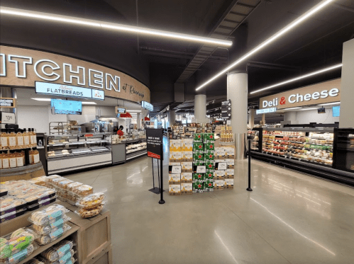 A modern grocery store interior featuring a deli, cheese section, and a flatbread counter with various products displayed.