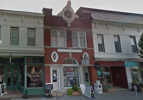 A quaint street view featuring a red brick building with a sign for "Berryville Old Book Shop" and neighboring shops.