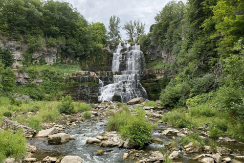 A scenic waterfall cascading down rocky cliffs, surrounded by lush greenery and a flowing river below.