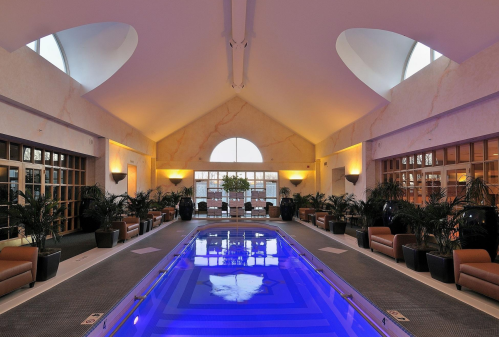 A serene indoor pool area with blue water, elegant lighting, and lush plants, creating a relaxing atmosphere.