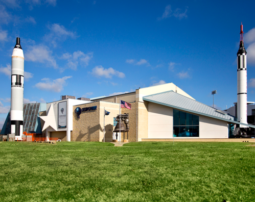 Exterior view of a space museum featuring rockets, a modern building, and a clear blue sky.