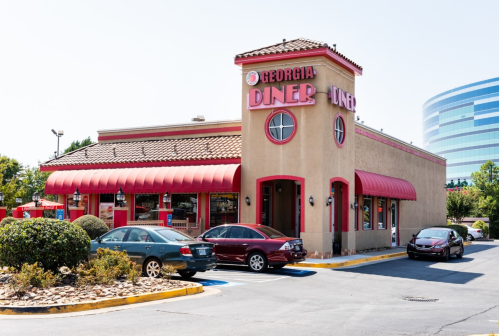 Exterior of Georgia Diner with a red awning, surrounded by cars and greenery on a sunny day.