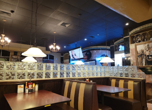 Interior of a restaurant featuring glass block walls, booths, and a large screen displaying a video.
