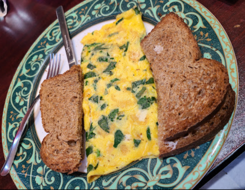 A plate with a spinach omelette and two slices of brown bread, accompanied by a fork and knife.
