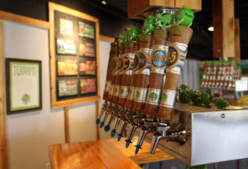 A row of beer taps with wooden handles, set against a rustic bar backdrop featuring framed artwork.