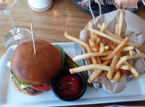 A juicy burger with lettuce, tomato, and a pickle, served with a side of crispy fries and ketchup on a wooden table.