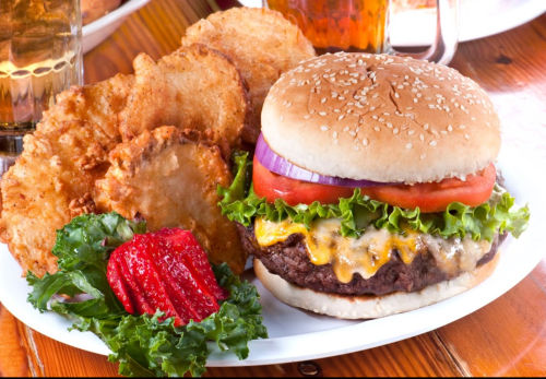 A juicy cheeseburger with lettuce, tomato, and onion, served with crispy potato wedges and a side of lettuce.