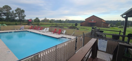 A serene outdoor pool surrounded by red and white chairs, with a barn and green fields in the background.