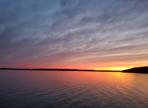 A serene sunset over calm waters, with vibrant hues of orange, pink, and purple reflecting on the surface.