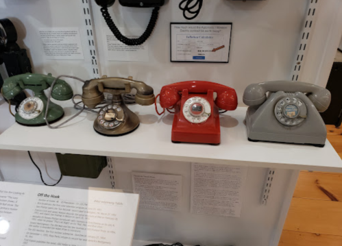 A display of vintage rotary phones in green, brown, red, and gray on a shelf.