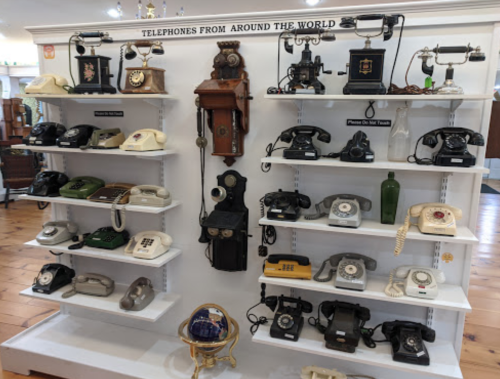 A display of various vintage telephones from around the world, arranged on a white wall shelf.