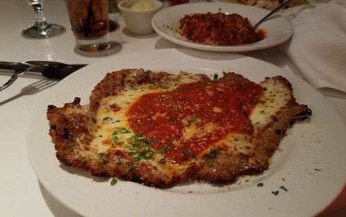 A plate of breaded chicken topped with marinara sauce and melted cheese, garnished with herbs.