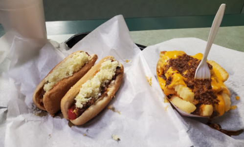 Two hot dogs with toppings and a side of cheesy chili fries on a tray.
