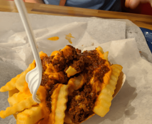 A bowl of crinkle-cut fries topped with chili and melted cheese, served with a plastic fork.