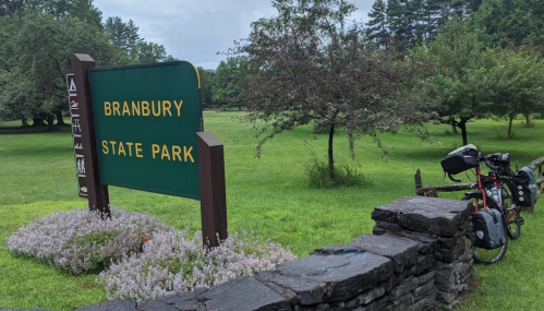 Sign for Branbury State Park with a bicycle parked nearby, surrounded by green grass and trees.