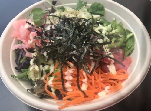 A colorful salad bowl with mixed greens, sliced vegetables, pickled ginger, and seaweed on top.