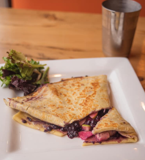 A folded crepe filled with black beans and colorful vegetables, served with a side salad on a white plate.