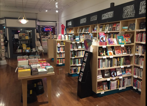 A cozy bookstore interior with wooden shelves filled with books, featuring sections for fiction, mystery, and sci-fi.
