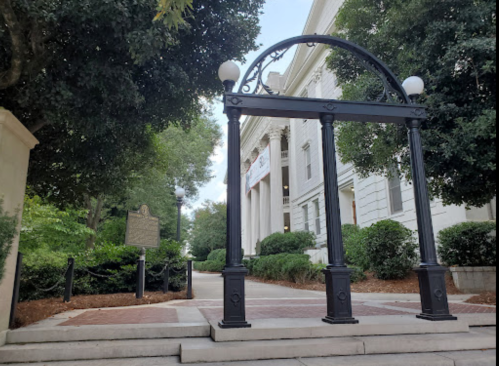 Archway structure in front of a historic building, surrounded by greenery and a marker on the left.