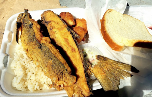 A takeout container with fried fish, rice, a side of coleslaw, and a slice of bread.