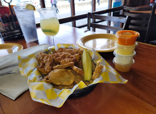 A basket of fried chicken and pickles, with dipping sauces and a margarita on a wooden table.