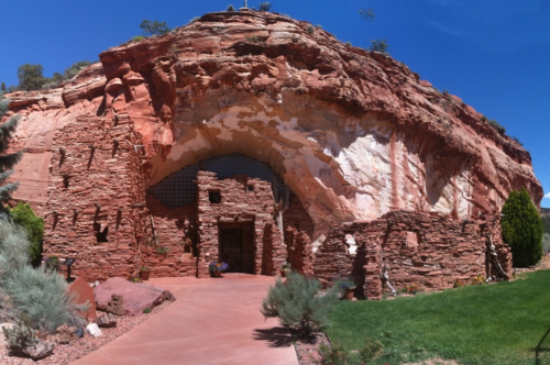 A unique rock formation with a cave-like entrance, surrounded by greenery and blue sky.