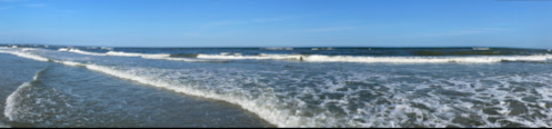 A panoramic view of a calm beach with gentle waves under a clear blue sky.
