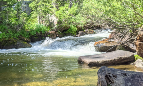 A serene river flows through a lush green landscape, with rocks and trees lining the banks.