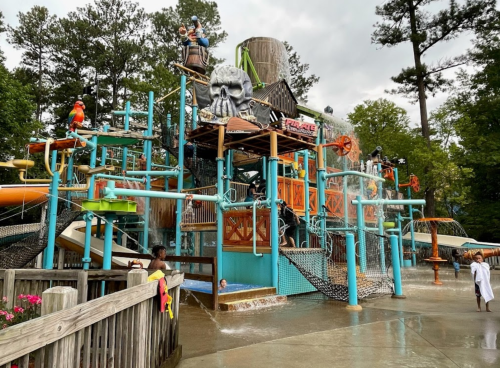A colorful water park play structure with slides, water features, and pirate-themed decorations on a cloudy day.