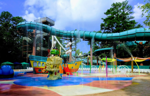 A colorful water park featuring a pirate ship, water slides, and splash areas under a blue sky.