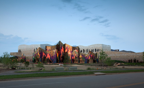 A modern building with colorful, abstract patterns on its facade, surrounded by greenery and a clear blue sky.