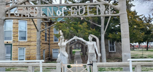 Entrance to the Garden of Eden, featuring two sculptures of figures holding hands under a wooden archway.